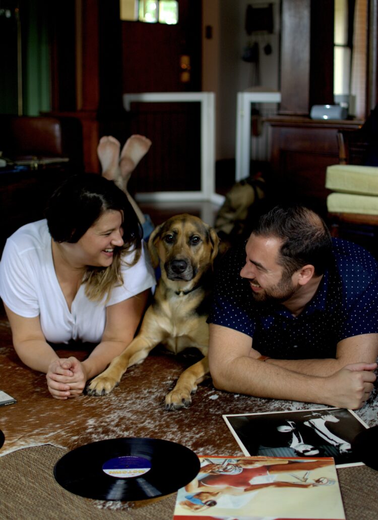 This is a photo by Kat Stano of a young couple lounging on the floor in their stylish home, with their dog, looking at vintage vinyl records.