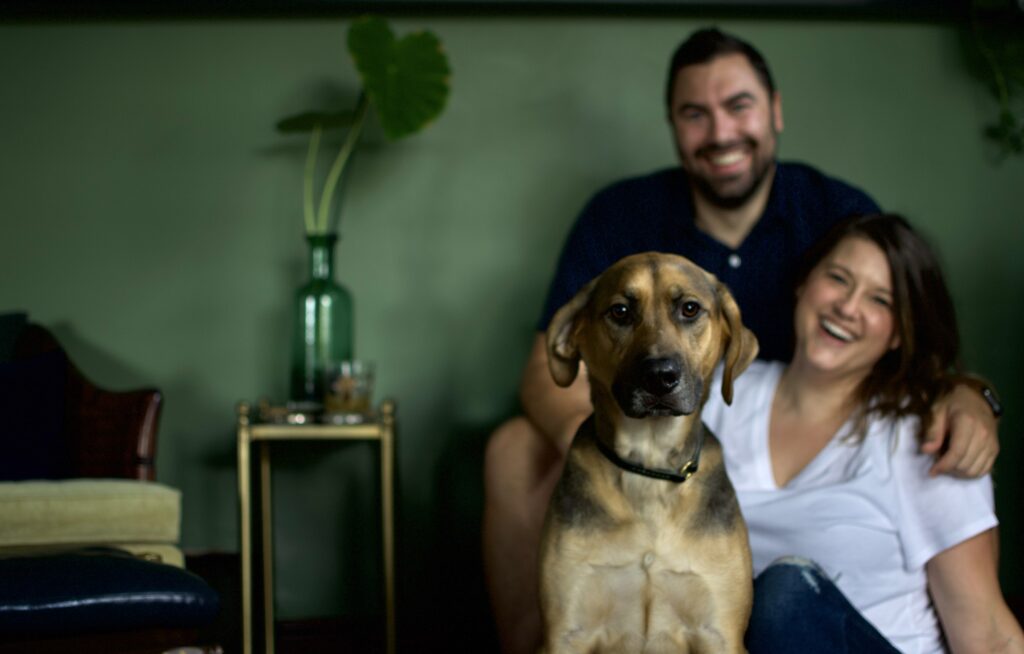 This is a cute couple laughing in the background while their dog takes center stage as an example of date night ideas at home.