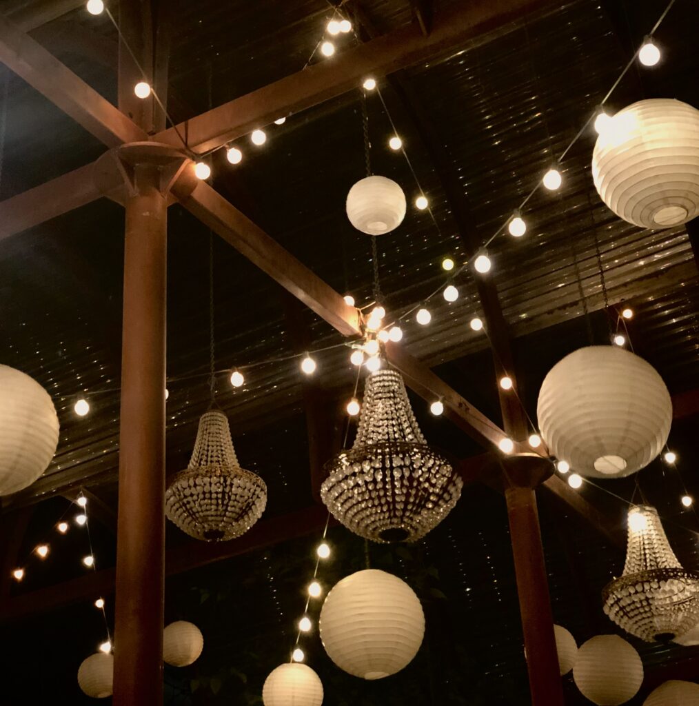 This is a photo of an event space with lanterns, twinkle lights, and crystal chandeliers. 