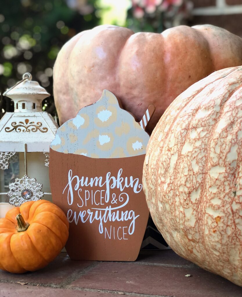 This is a photo of a fall front porch vignette with pumpkins, a lantern, and a sign that says, "Pumpkin spice and everything nice."