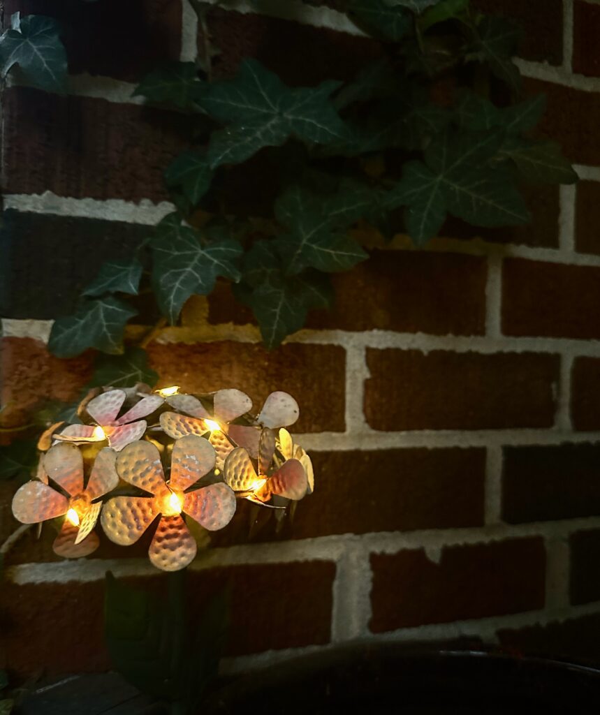 This is a photo of a metal garden flower with twinkle lights glowing on the front porch.