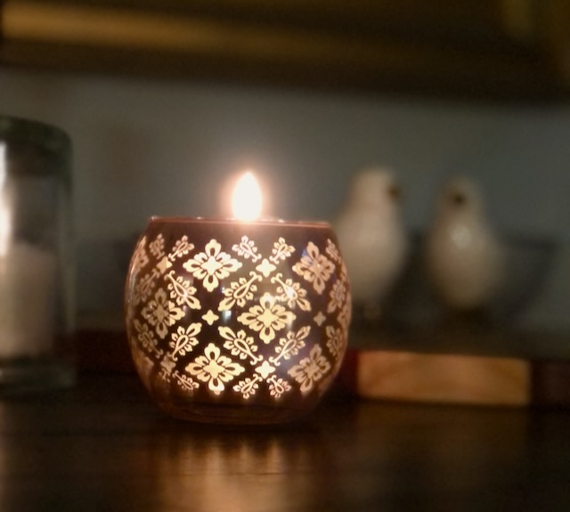 This is a picture of a glowing candle in a lace-fringed votive to illustrate how to make your home eco friendly.