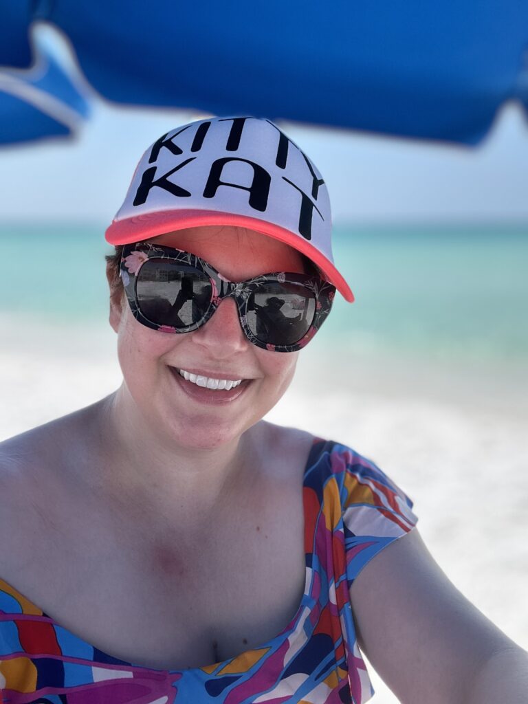 This is a photo of Kat Stano on the beach with a hat that says "Kitty Kat."