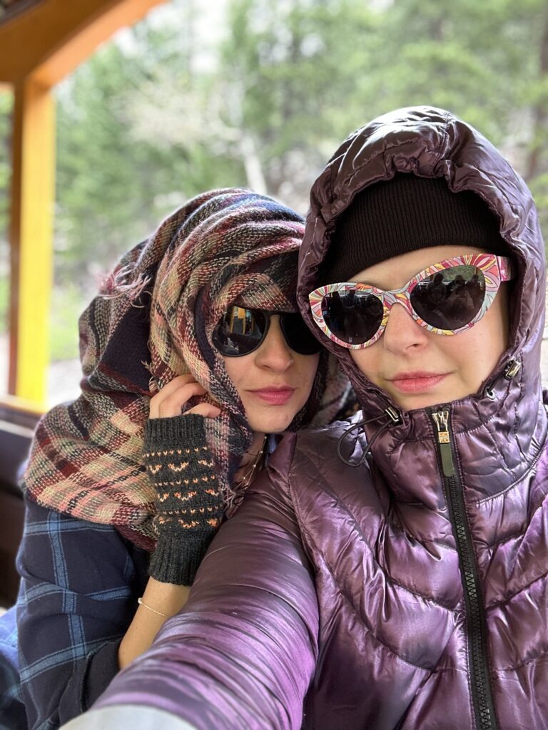 This is a photo of Kat and her friend wearing sunglasses, hats, and scarves, and looking kind of suspicious.