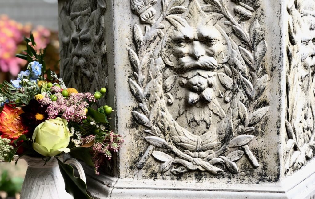 This is a vase of flowers by a gothic, greek stone statue as ideas on greek stone statues in your garden.