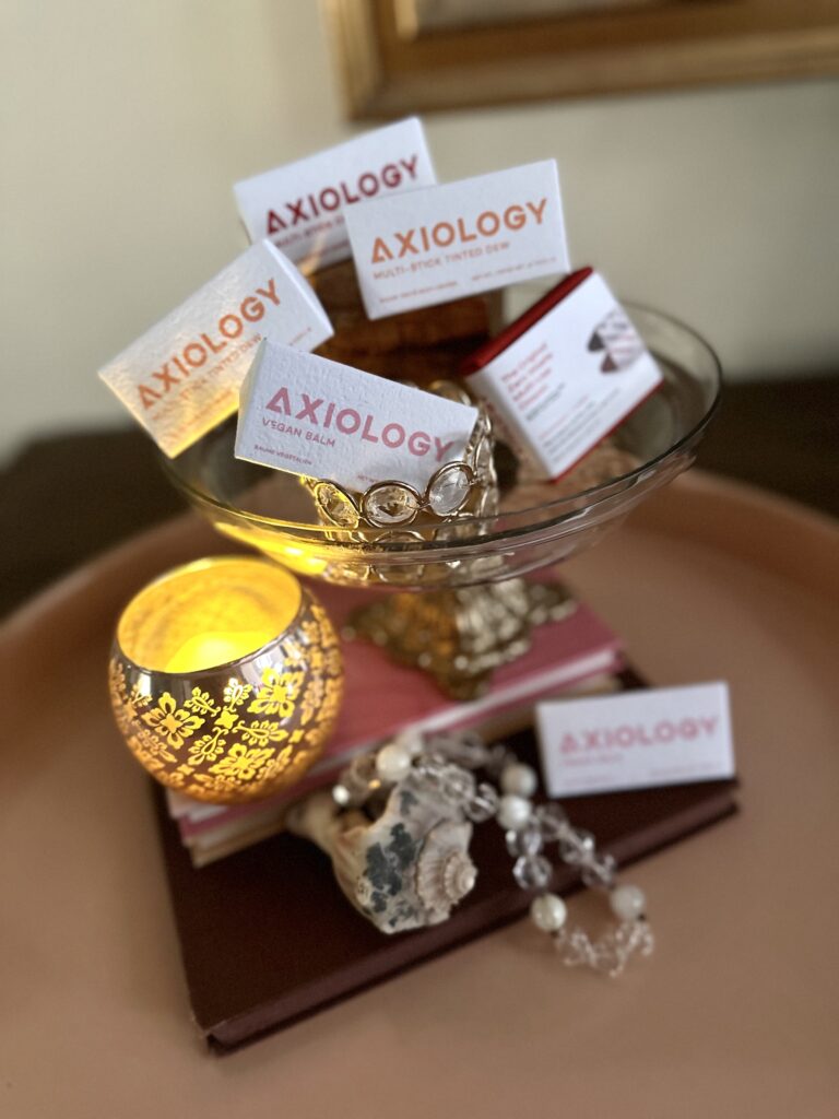 This is a photo of zero-waste makeup in a glass container with a candle, seashell, necklace, and books.