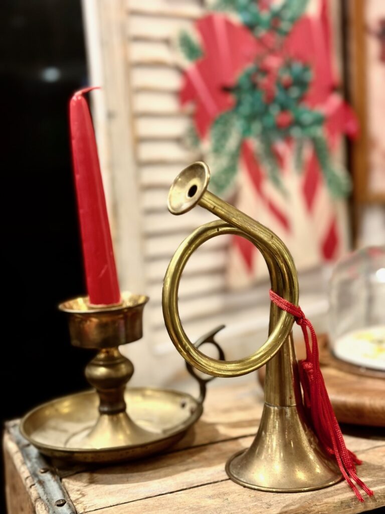 This is a vintage brass candle holder with a red tapered candle and a vintage brass horn as examples of sustainable christmas market decorations.