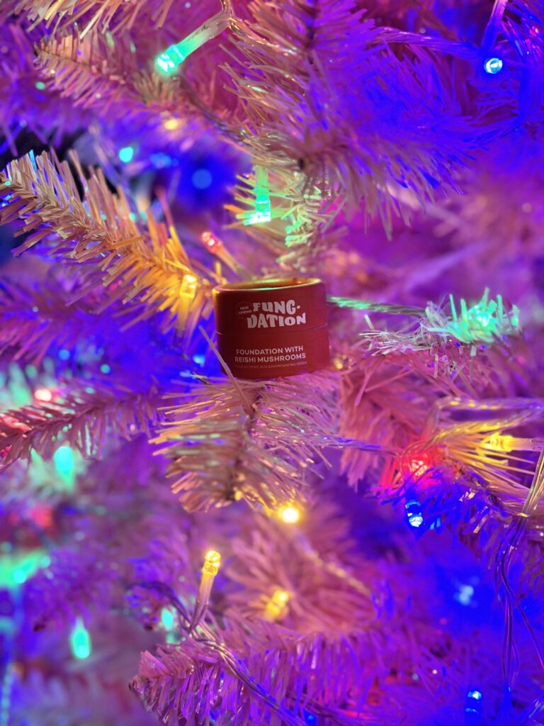 Here's the red container of Fungdation sitting in a pink and colorfully-lit Christmas tree to show vegan foundation brands.