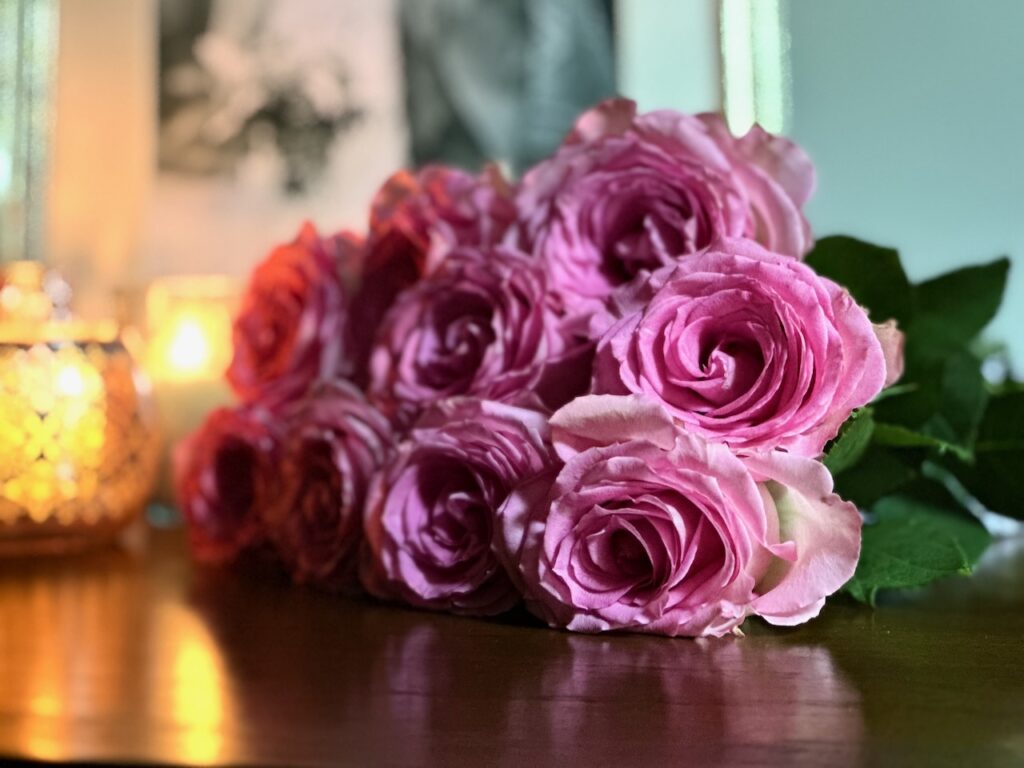 This is a photo by Kat Stano of a beautiful bouquet of purple roses on a table with candles as an advantage of kindness.