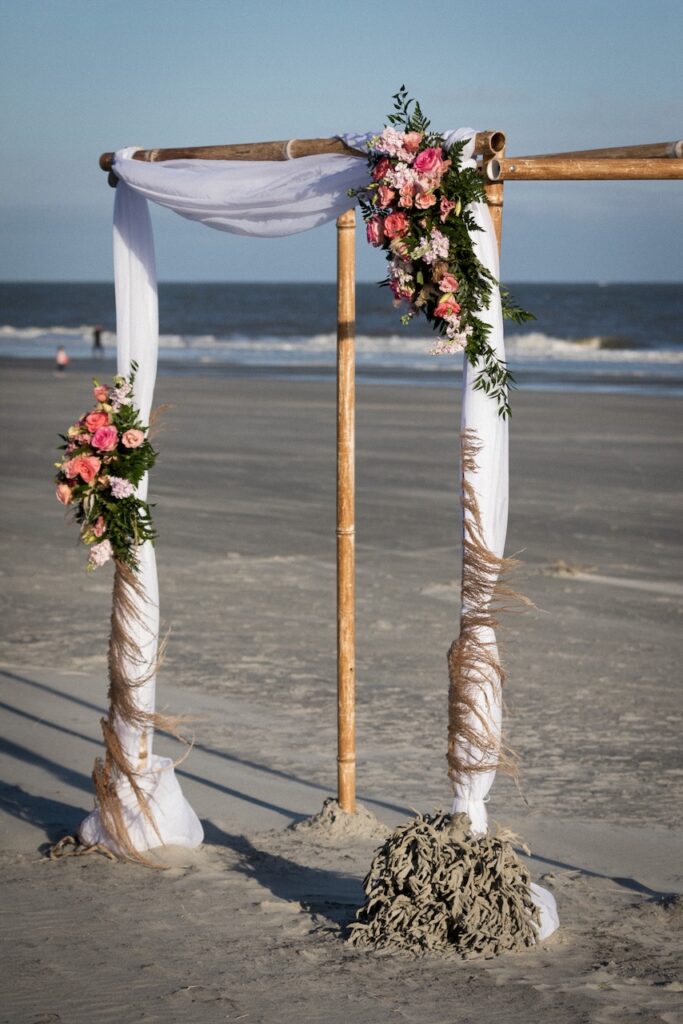 This is a wedding arbor on the beach with draping and colorful flowers to show eco friendly wedding venues.