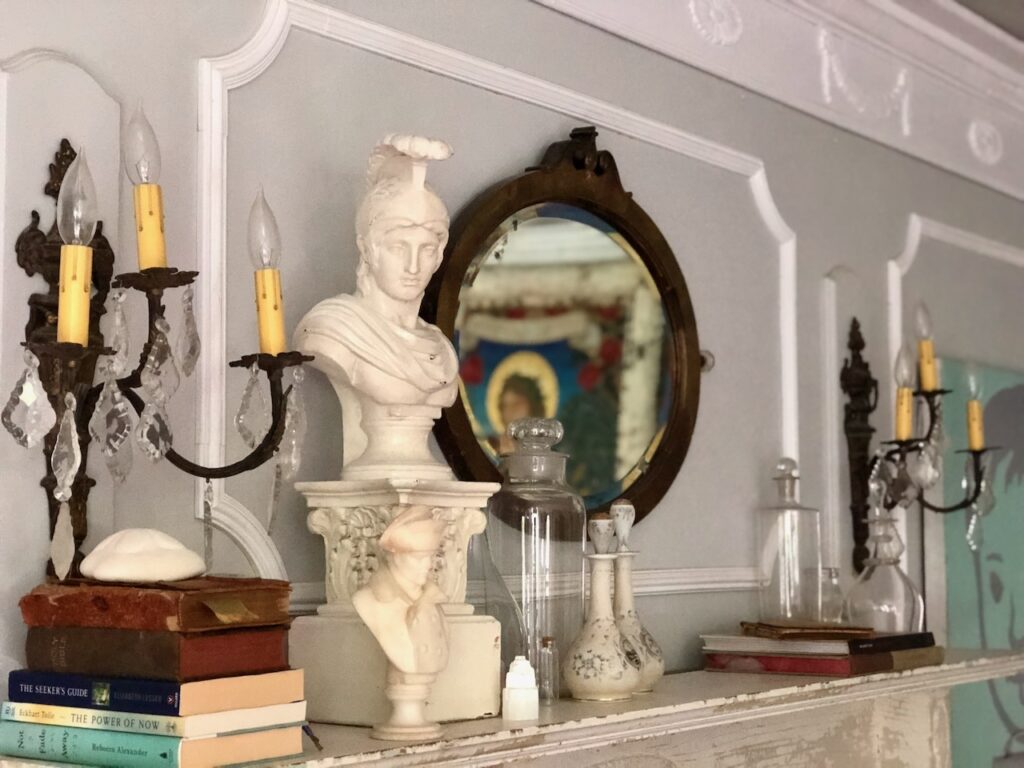 This is a mantel with antique elements like books, sconces, statues, vases, and a retro mirror to demonstrate vintage wedding shops near me.