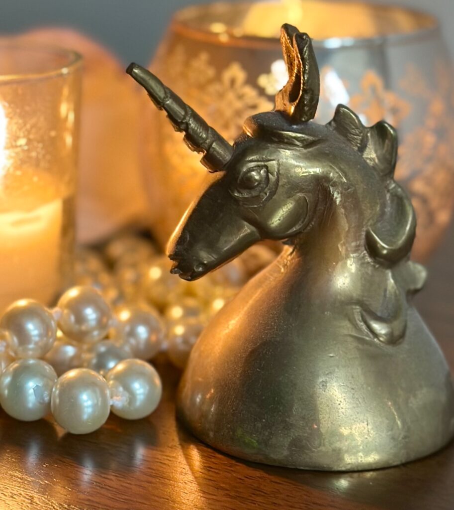 This is a brass unicorn hand bell with candles and pearls next to it to show indoor wedding send off ideas.