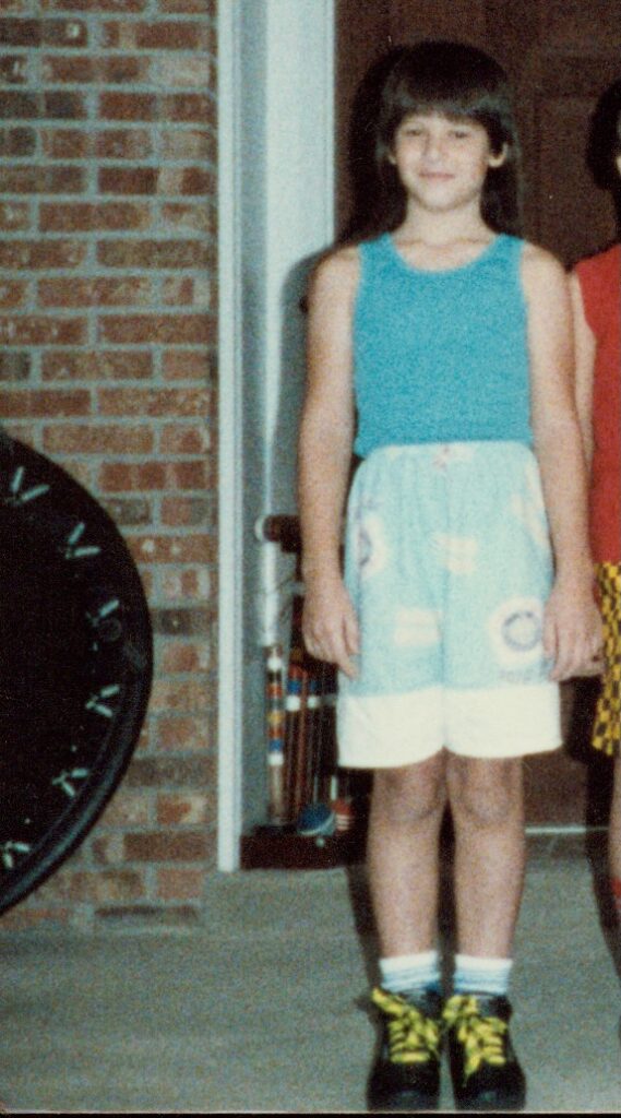 This is Kat as a little girl on her front porch, wearing a turquoise tank top, jams, also known as long, graphic shorts, socks, and black shoes with neon shoelaces, plus a mini trampoline and croquet set in the background to share ideas for this article on business card holder diy.