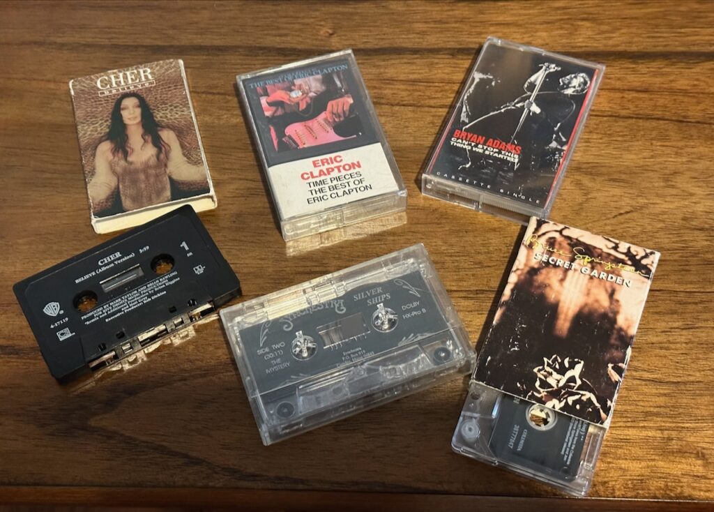 This is a collection of cassette tapes including performers Cher, Eric Clapton, Bryan Adams, Bruce Springsteen Secret Garden, and Synchestra Silver Ships to point out card case pattern.