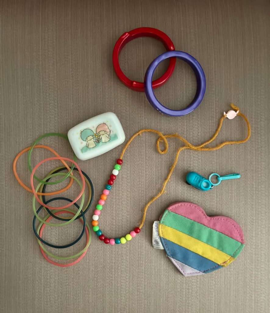 This is a flat-lay photo of Kat's '80s memorabilia, including bangle bracelets, jelly bracelets, a Twin Stars soap case, a homemade rainbow-colored beaded necklace, a turquoise roller skate charm, and a striped rainbow heart coin purse to show ideas on how to make a business card holder.