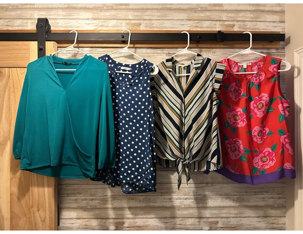 This is a teal long-sleeve blouse, navy polka dot sleeveless blouse, striped sleeveless blouse, and red floral sleeveless blouse hanging from a barn door rail to discuss what colours can you wash together for a do laundry blog post.