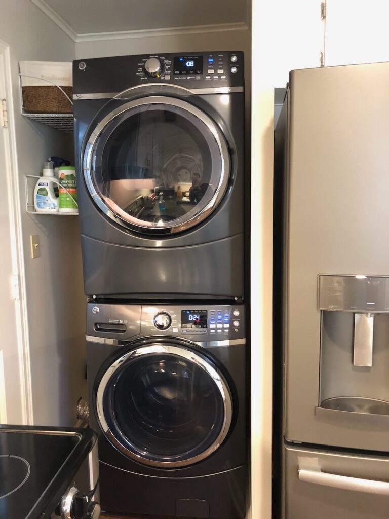 This is a laundry alcove with a front loading washer and dryer stacked, squeezed between two small shelves, a back door, fridge, and stove for a discussion on how to do eco friendly laundry, including how to do laundry in college.