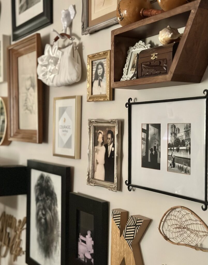 This is Kat's gallery wall with shelves, little boxes, musical maracas, photos of family members, artistic drawings, Kat's wedding purse on an elephant hook, a handmade dream catcher made by Kat's late brother, and a seashell to show home decor inspo.
