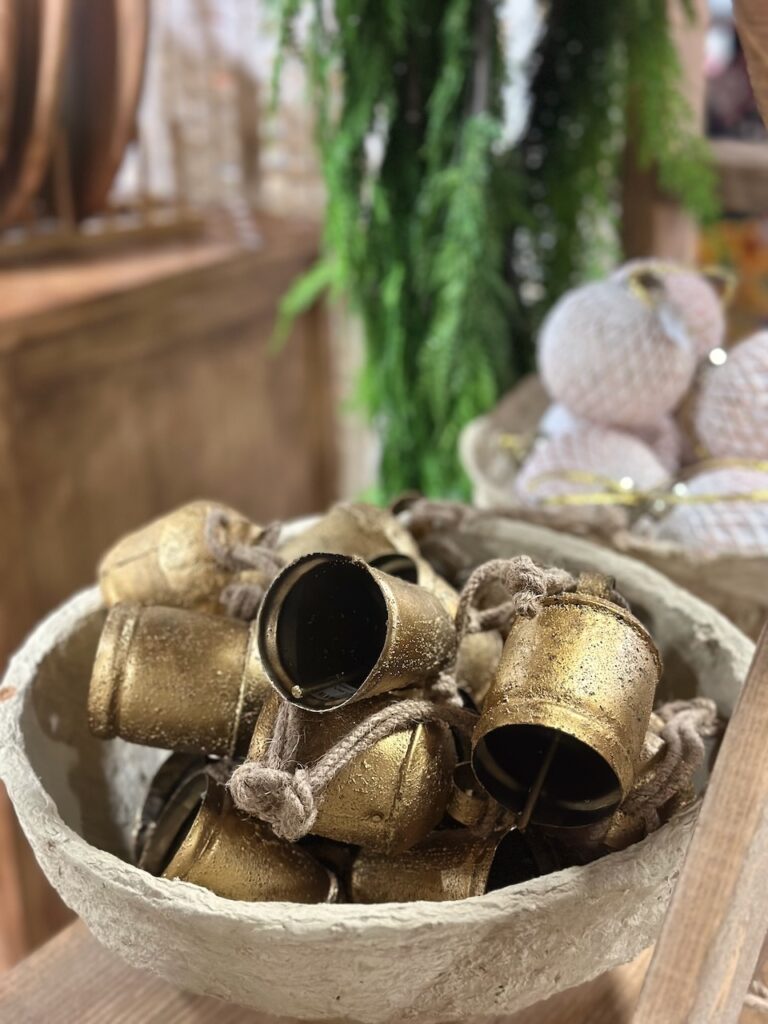 These are cute brass bells in a wooden bowl with ball ornaments and garland in the background to show eco friendly baubles.