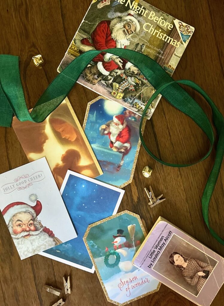 This is a vignette flatlay of the book "'Twas the Night Before Christmas" and the book "Little Women" plus greeting cards, wooden clothespins, green ribbons and jingle bells to show eco friendly christmas decorations diy.