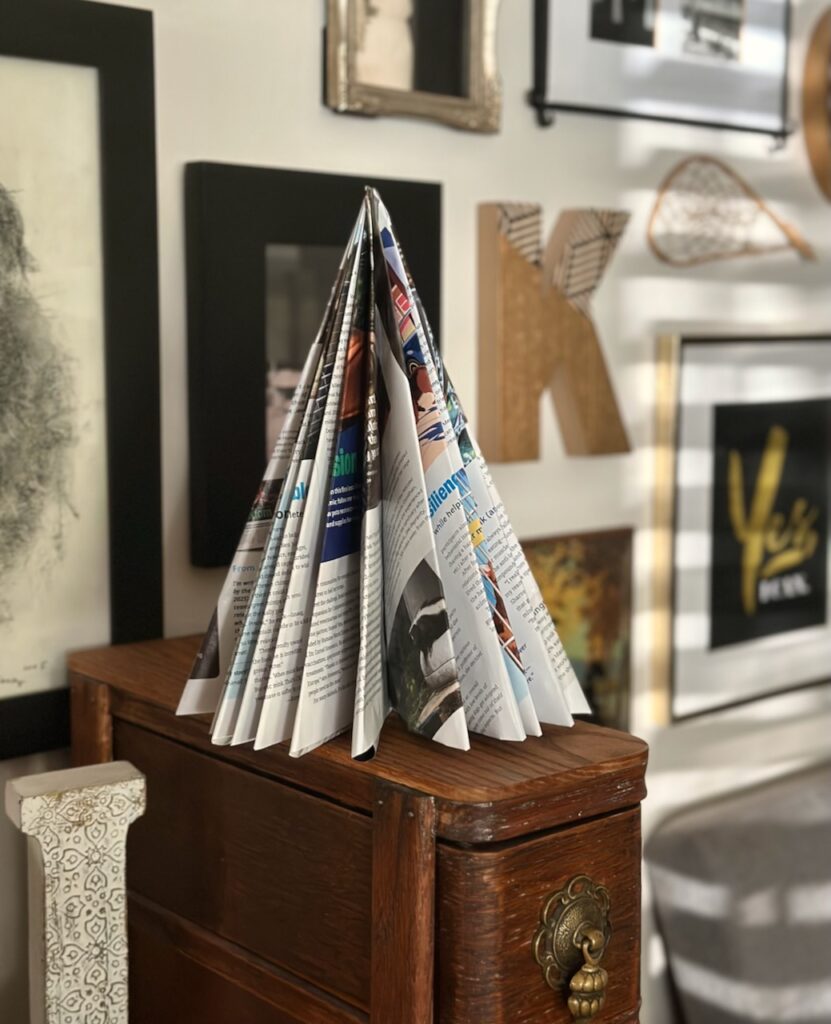 This is a paper Christmas tree made out of a catalog that's sitting on sewing machine drawers in front of a gallery wall to show sustainable Christmas decorations.