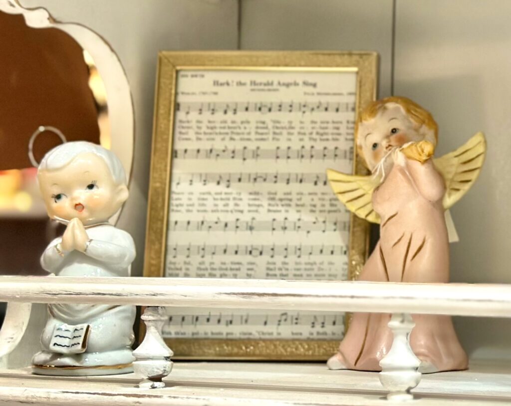 This is the sheet music "Hark the Herald Angels Sing" framed in a gold frame next to two sweet angel figurines to show sustainable christmas decorations diy.
