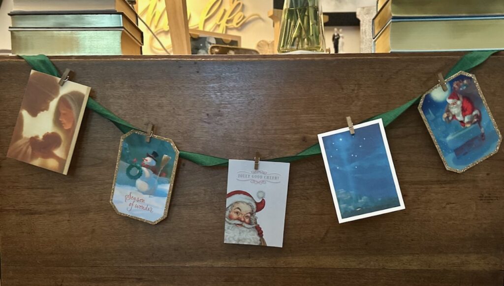 This is a group of Christmas cards attached to a ribbon with wooden clothespins hanging across an antique table to show christmas decorations eco friendly.