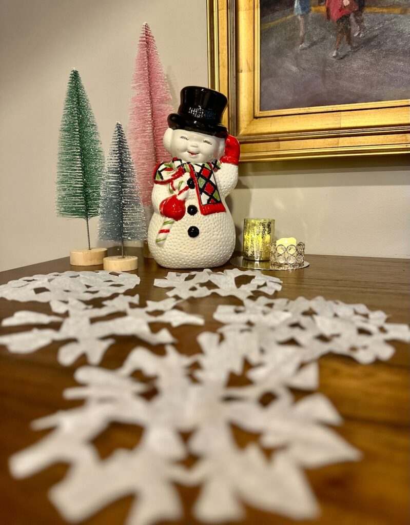 This is a handmade ceramic snowman from the 1980s, bottlebrush trees, and coffee filter hand-cut snowflakes to show compostable ornaments.