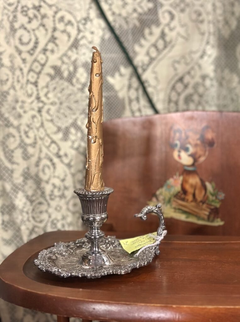This is a silver vintage candle holder with a gold candle sitting on a vintage wooden high chair with a lace backdrop to show eco friendly christmas decoration.