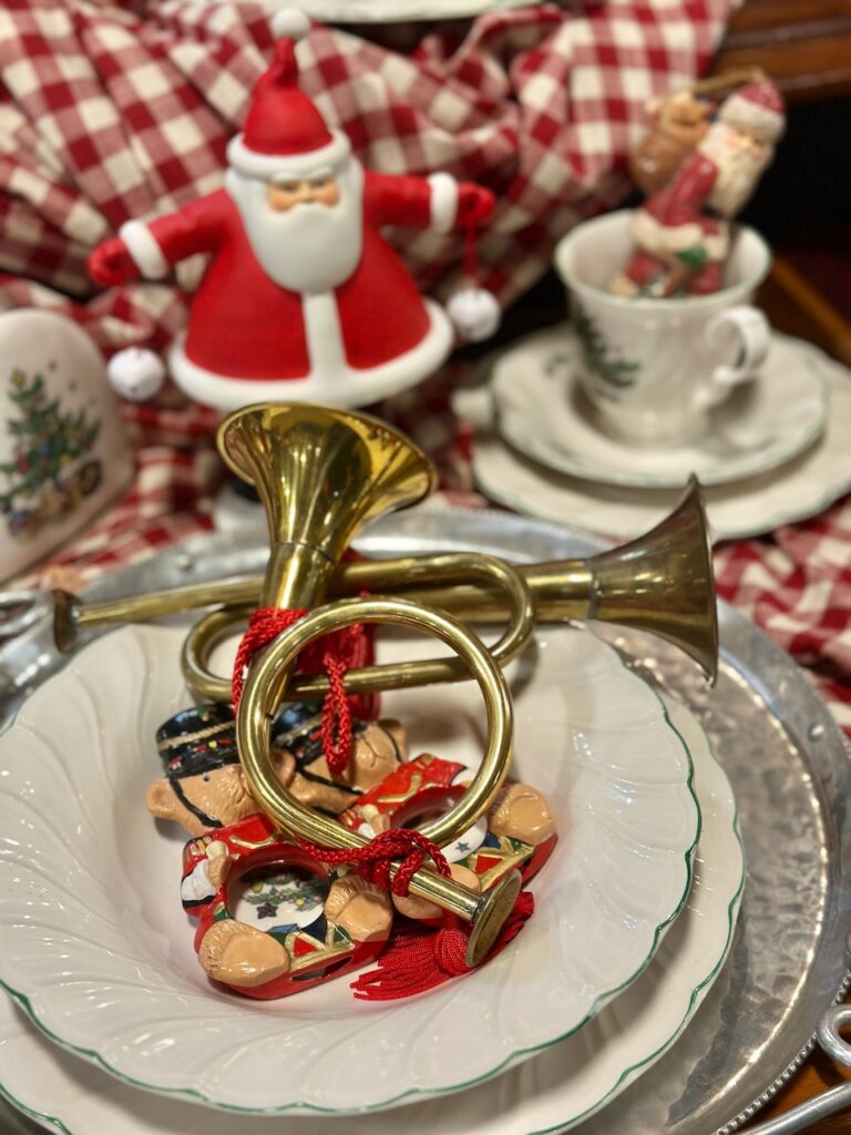 This is a vignette for Santa figurines, Christmas cup and saucer, vintage instrument horn, ornaments, and plates to show greening christmas.