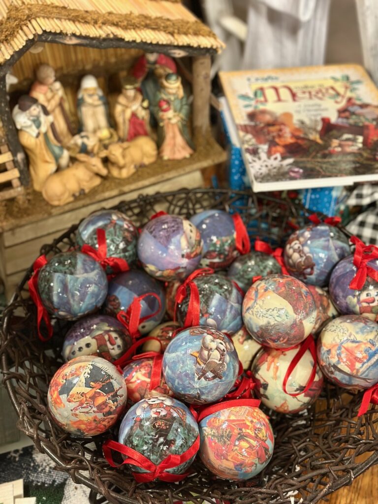 This is a nativity scene, a holiday book, and a basket full of ball ornaments with colorful scenes to show sustainable outdoor christmas decorations.